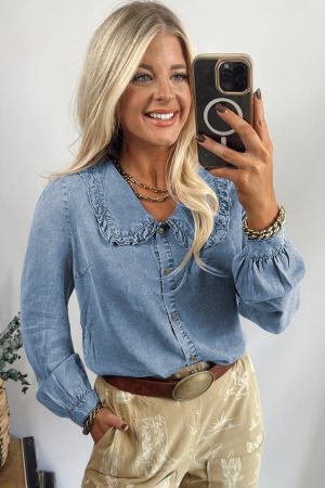 Smiling woman taking a mirror selfie wearing a light blue denim shirt with a ruffled collar and long sleeves