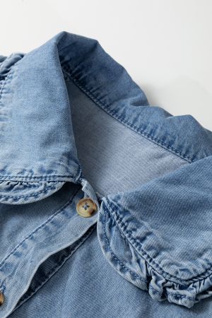 Close-up of the collar of a light blue denim shirt with ruffles and a button, highlighting fabric texture