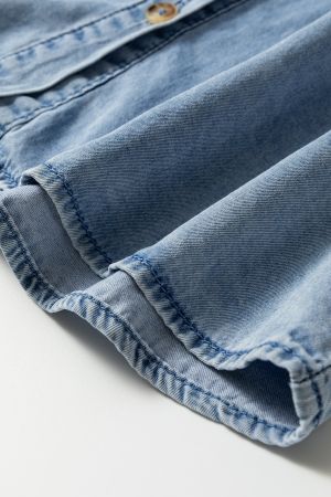 Detail of light blue denim shirt fabric, showing soft denim texture and fine stitching