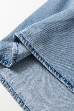 Close-up of the hem of a light blue denim shirt with visible stitching and classic denim finish